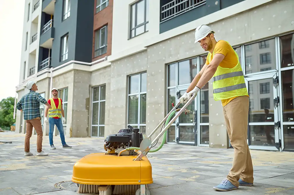 Arbeiter, der eine Baustelle reinigt, und zwei Männer in der Nähe des Gebäudes